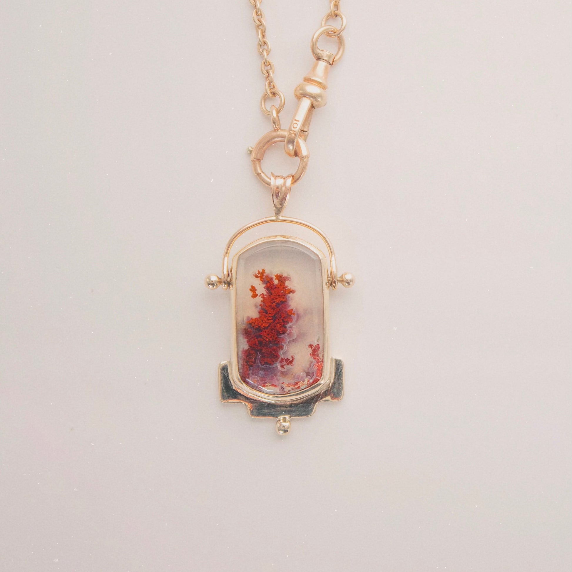 Necklace with a pendant featuring red and gold 
colors on a light gray background