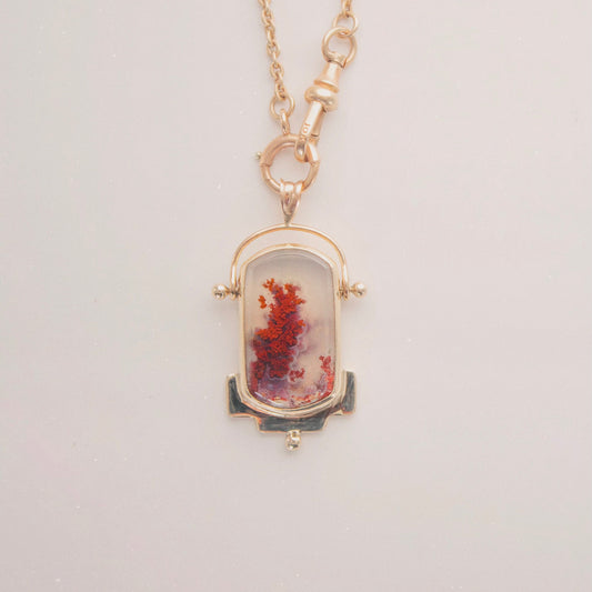Necklace with a pendant featuring red and gold 
colors on a light gray background