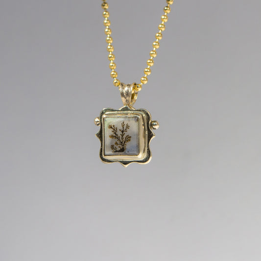 Gold necklace with a square pendant featuring a botanical design on a gray background