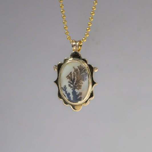 Gold necklace with a pendant featuring a natural scene on a gray background