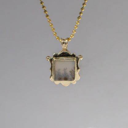 Gold pendant necklace with a gray stone on a gray background