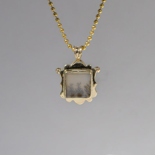 Gold pendant necklace with a gray stone on a gray background
