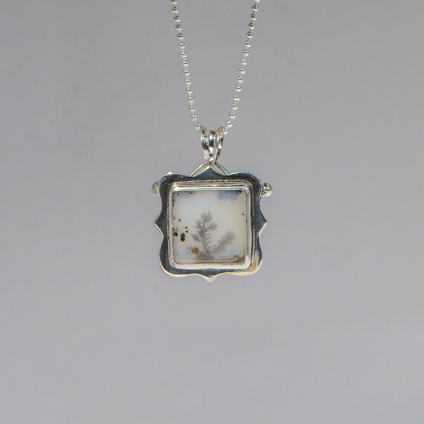 Silver pendant with a square design on a gray background