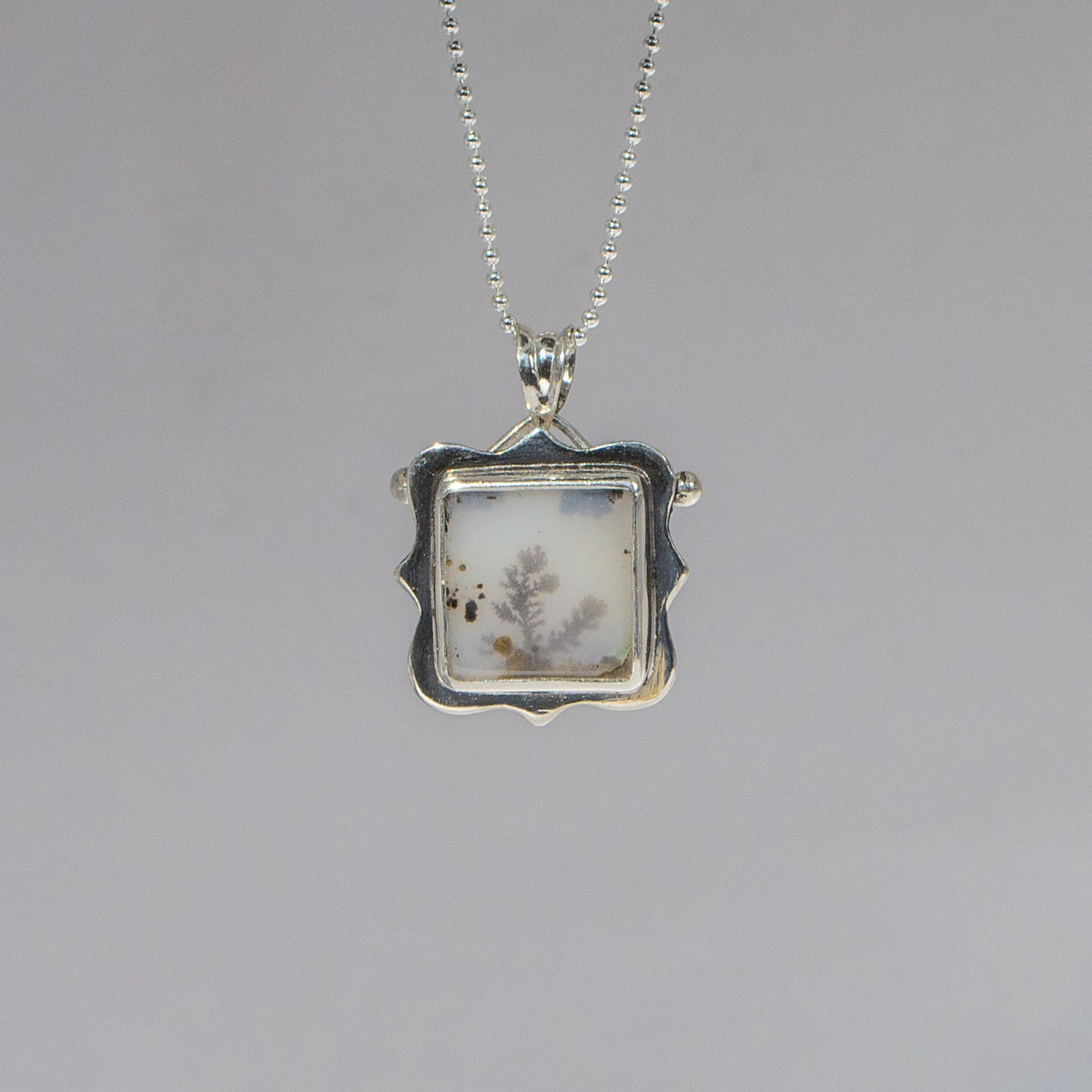 Silver pendant with a square design on a gray background