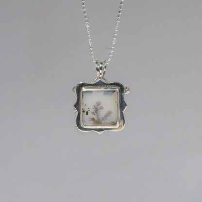 Silver pendant with a square design on a gray background