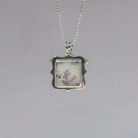 Silver pendant with a square design on a gray background