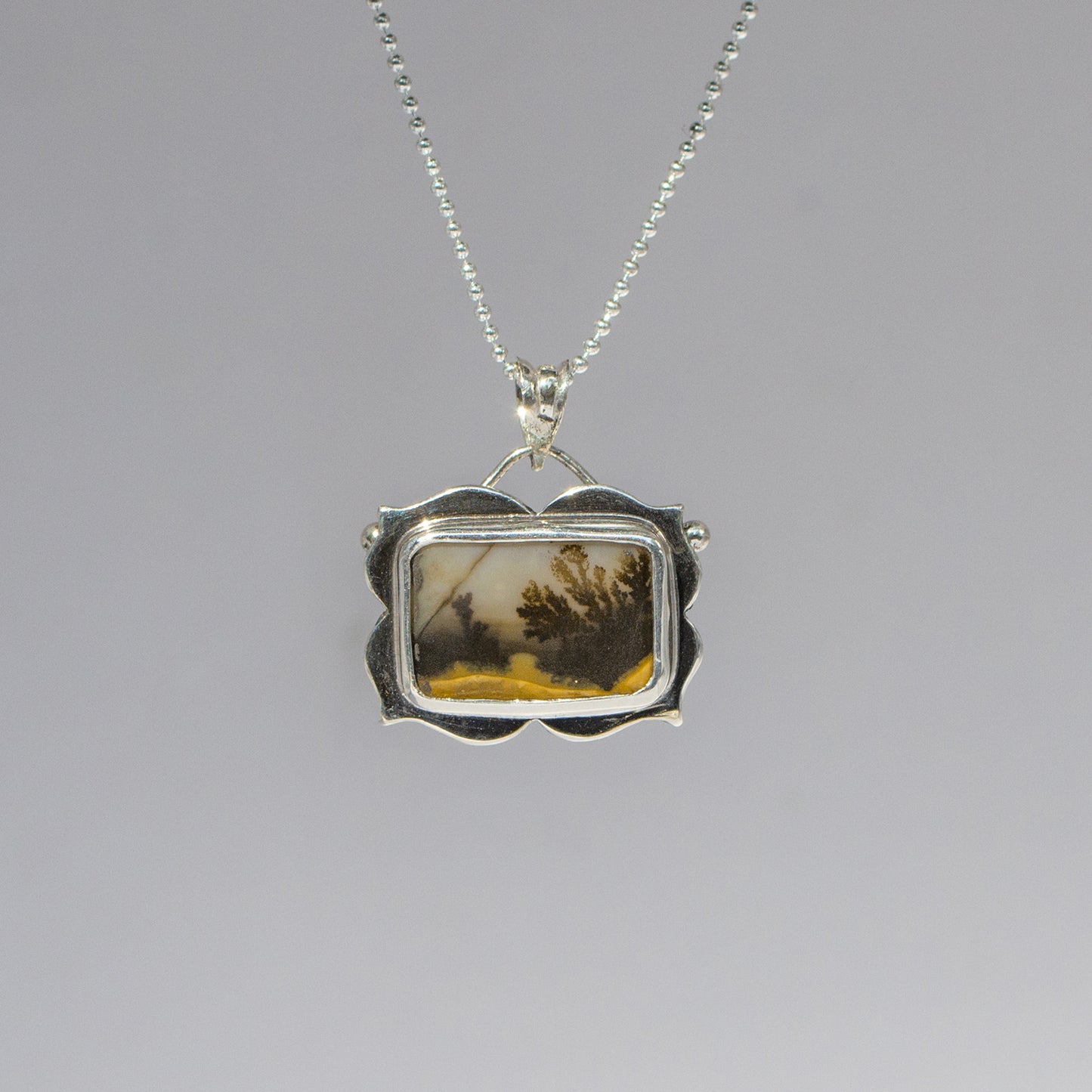 Silver pendant with a scenic design on a gray background