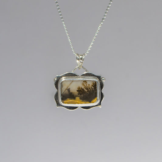 Silver pendant with a scenic design on a gray background