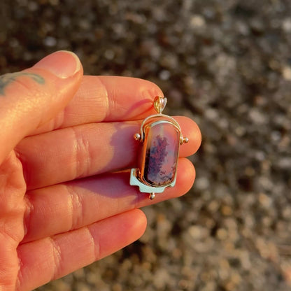 video showing gold charm shining in the afternoon sun being held by a hand.
