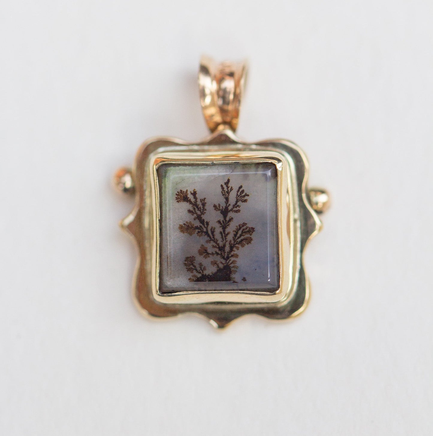 Gold pendant with a square stone featuring a natural design on a light gray background