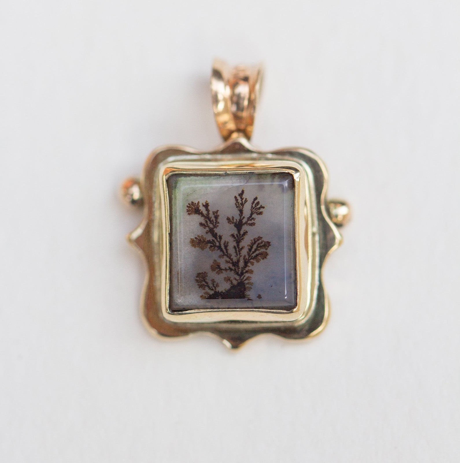 Gold pendant with a square stone featuring a natural design on a light gray background