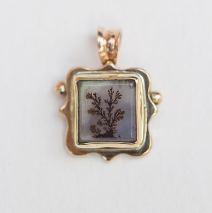 Gold pendant with a square stone featuring a natural design on a light gray background