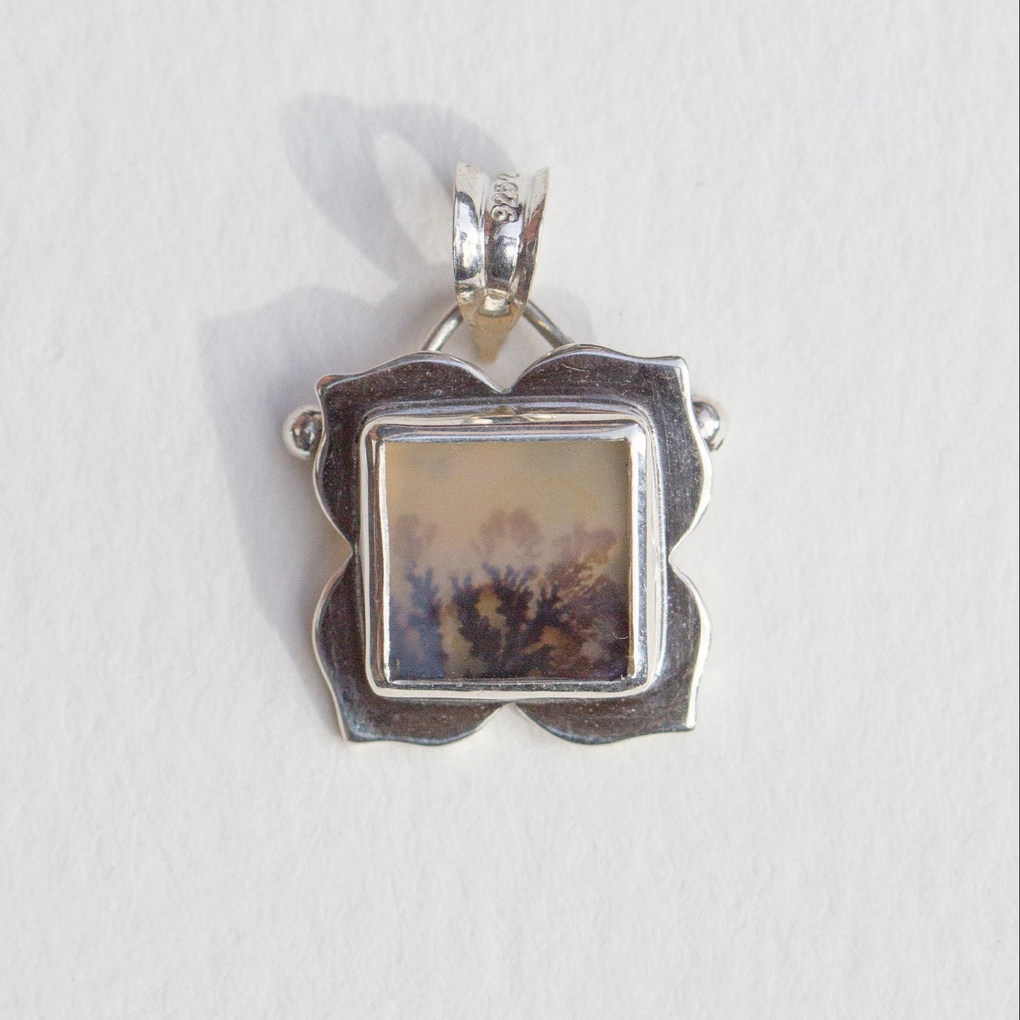Silver pendant with a square stone on a white background
