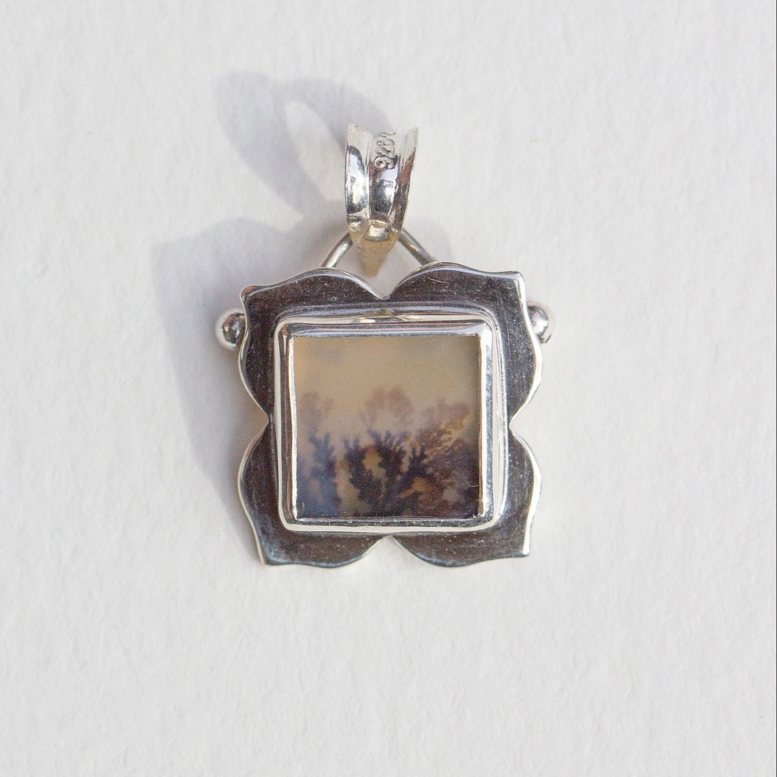Silver pendant with a square stone on a white background