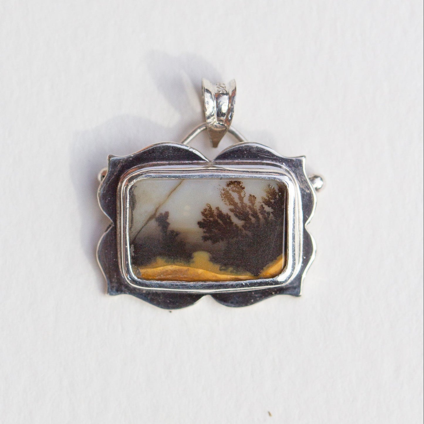 Silver pendant with a natural landscape design on a white background