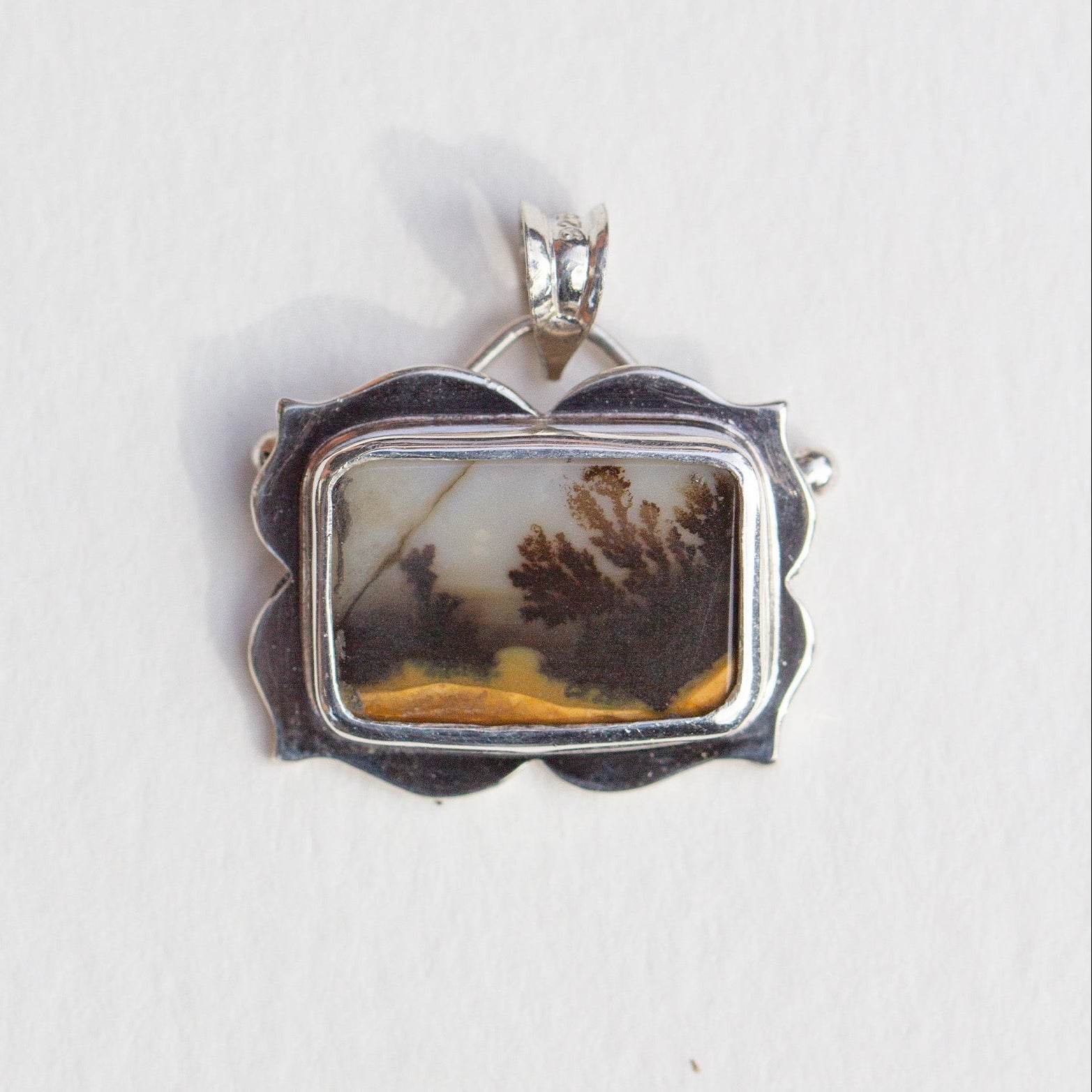 Silver pendant with a natural landscape design on a white background
