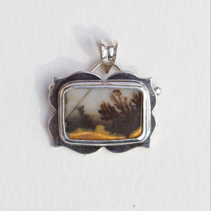 Silver pendant with a natural landscape design on a white background